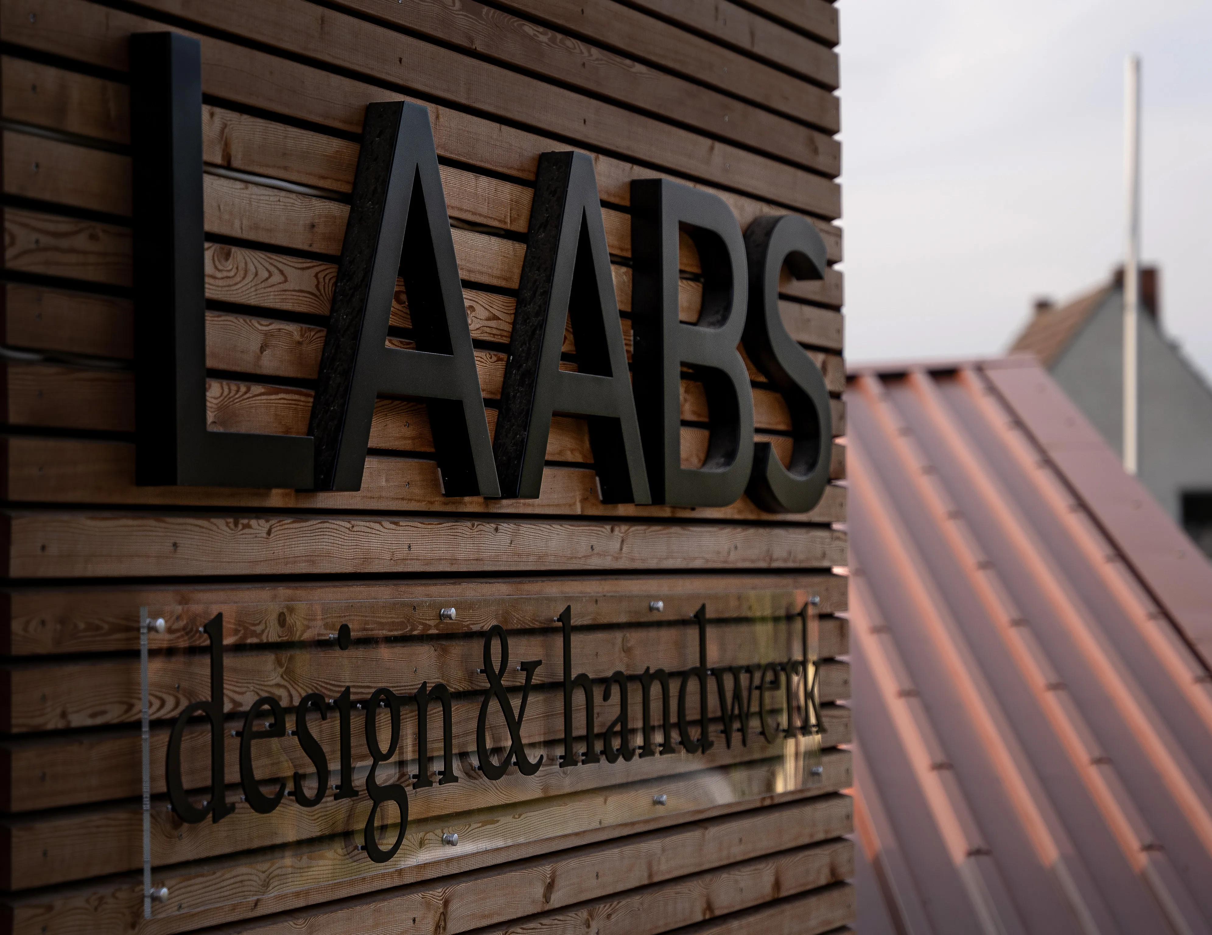 Das Firmenlogo von Laabs design & handwerk ist auf einer Holzfassade in großen schwarzen Buchstaben montiert und wirkt modern und hochwertig.