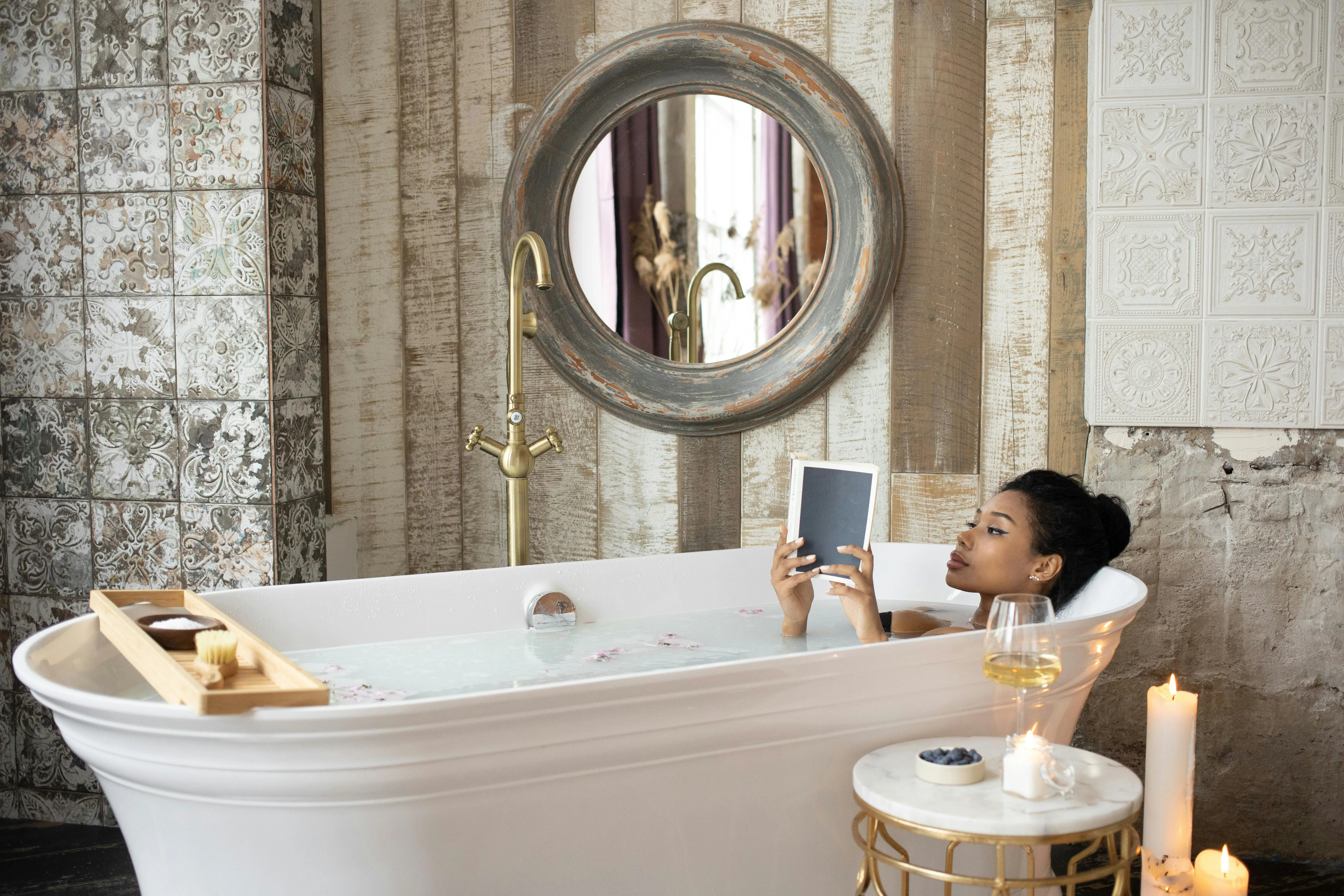 Eine Frau liegt in der Badewanne und genießt die Auszeit mit einem Buch und ein Glas Wein.