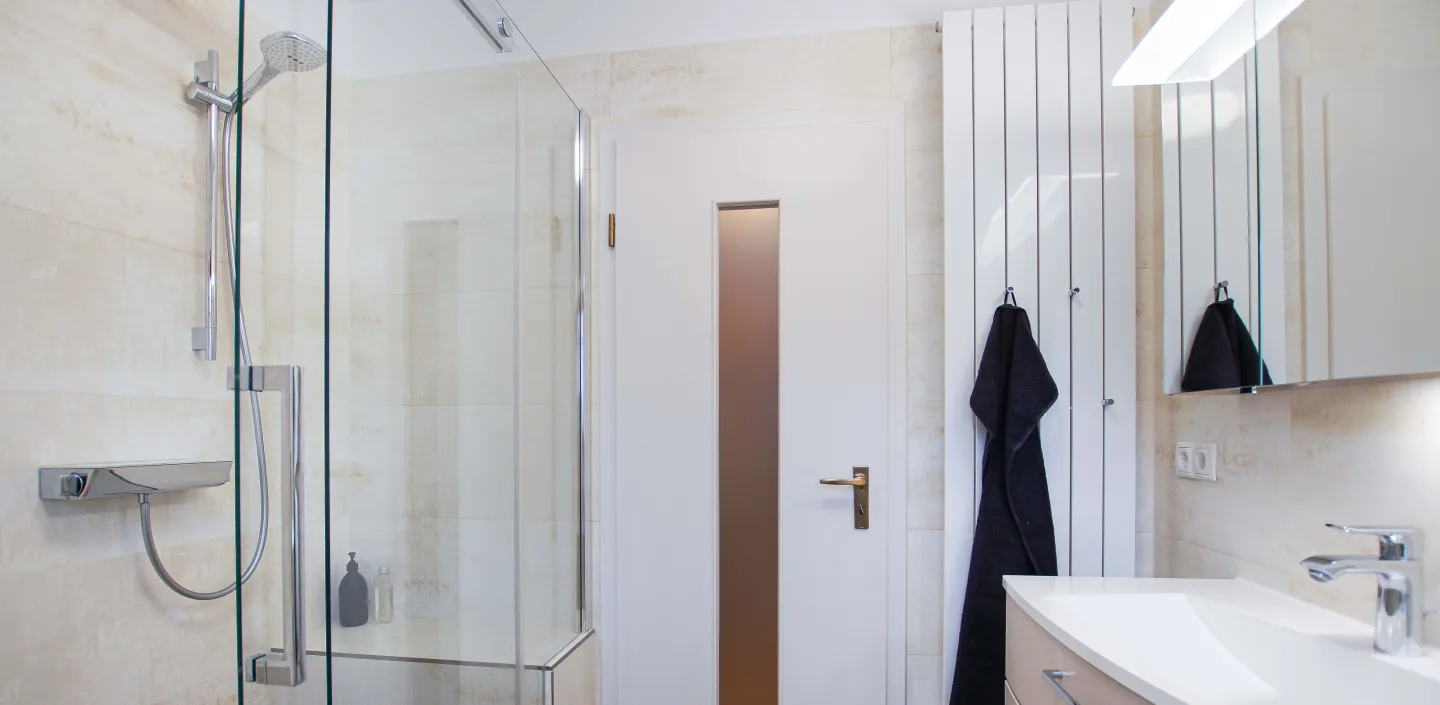 Badezimmer in beige mit begehbarer Dusche mit Schiebtür und Heizkörper mit Handtuchhaken.