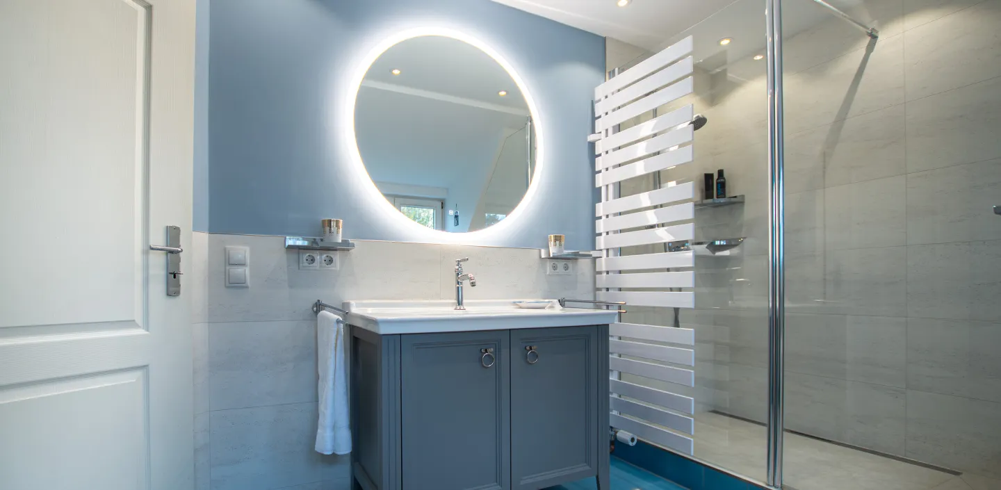 Matt grauer Waschtischanlage von Vitra mit rundem Lichtspiegel und begehbarer Dusche.