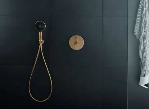 Ein luxuriöses Duschsystem mit einer goldenen Unterputzarmatur und einem schwarz-goldenen Duschkopf vor einer mattschwarzen gefliesten Wand.