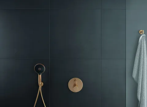 Ein luxuriöses Duschsystem mit einer goldenen Unterputzarmatur und einem schwarz-goldenen Duschkopf vor einer mattschwarzen gefliesten Wand.