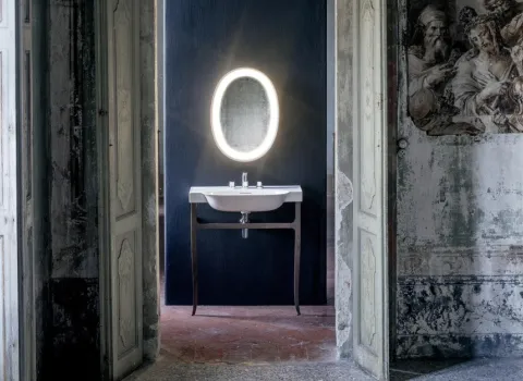 Ein stilvolles Badezimmer in einem historischen Gebäude zeigt ein modernes Waschbecken mit filigranen Beinen vor einer dunklen Wand.