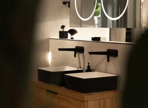 Zweifarbiger Doppelwaschtisch mit schwarzen Wandarmaturen und Hängespiegel.