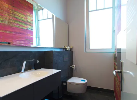 Einblick in ein Gästebad mit bunter Tapete, großem Spiegel, dunkler Armatur und einem Dusch-WC.