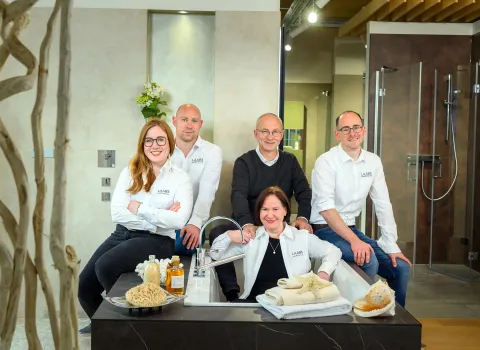 Gruppenbild der Familie Laabs, sitzend um eine Badewanne, in der Badausstellung von Laabs GmbH für Heizung, Sanitär und Fliesen.
