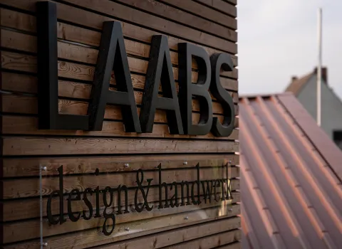 Das Firmenlogo von Laabs design & handwerk ist auf einer Holzfassade in großen schwarzen Buchstaben montiert und wirkt modern und hochwertig.