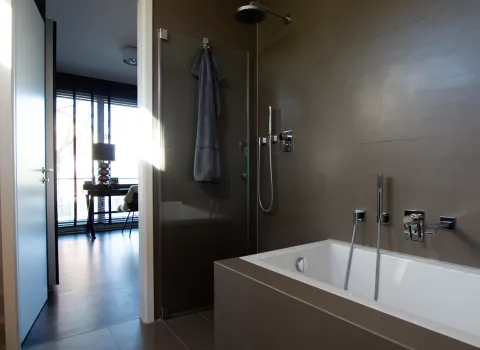 Blick in das nächste Zimmer aus einem Durchgangsbad mit Badewanne und Dusche vom Handwerksunternehmen bad & heizung Laabs in Potsdam.