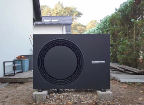 Luft-Wasser-Wrmepumpe in schwarz von Buderus stehend auf einem Podest im Garten.