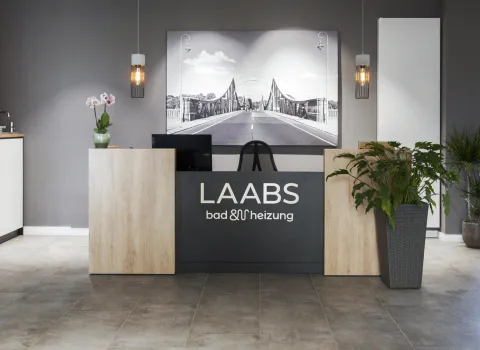 Ausstellung von Laabs bad & heizung zeigt ein modernes Design eines stilvollen Empfangsbereichs mit natürlichen Materialien, Pflanzen und einer eleganten Ausstellung hochwertiger Armaturen.