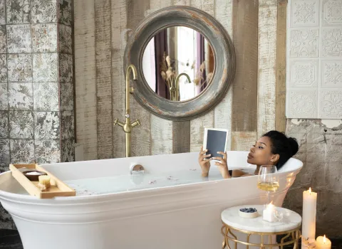 Eine Frau liegt in der Badewanne und genießt die Auszeit mit einem Buch und ein Glas Wein.