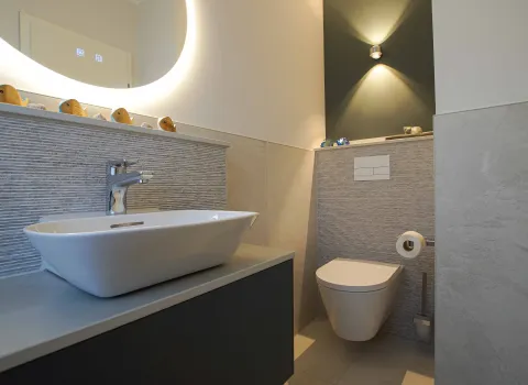 Gästebad mit Aufsatz-Waschtisch und WC mit rundem Lichtspiegel.