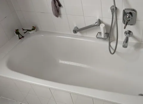 Ausschnitt aus dem alten Badezimmer mit Badewanne in weiß und weißen Fliesen.