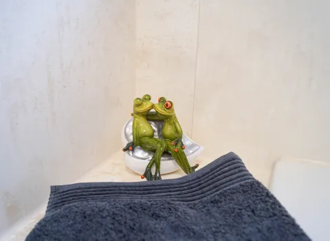 Wannenrandablage mit einem dunkelgrauen Handtuch und einer Dekofigur mit 2 küssenden Fröschen.