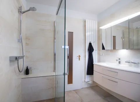 Komplettbad mit asymmetrischen Waschtisch und Spiegelschrank, sowie begehbarer Dusche mit Schiebetür.