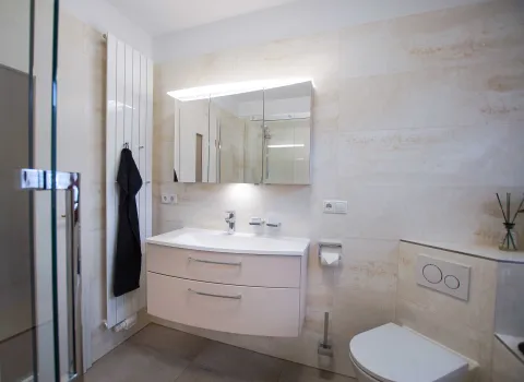 Asymmetrische Waschtischanlage mit 3-teiligem Spiegelschrank und Heizkröper mit Handtuchhaken. 