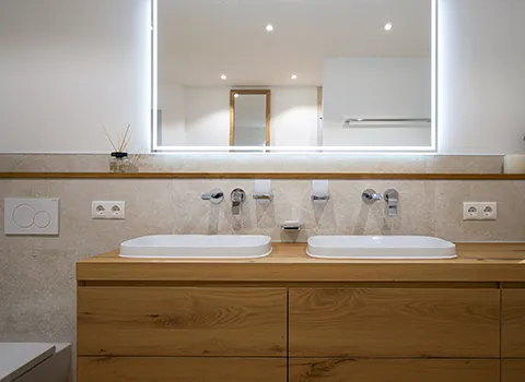 Doppelwaschtisch mit zwei integrierten Waschbecken und Holz-Unterschrank mit zwei Schubladen - dazu passend ein Lichtspiegel.