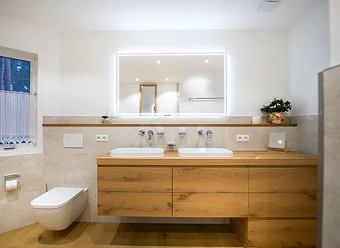 Doppelwaschtisch mit großem Unterschrank in Holzoptik mit großem beleuchteten Spiegel und wandhängendes WC.