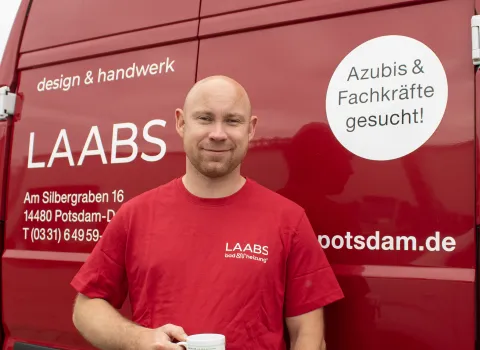 Mitarbeiter mit Kaffeetasse vor einem Transporter stehend. 