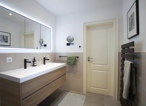 Elternbadezimmer mit IDEA Doppelwaschtisch und schwarzen Armaturen von hansgrohe und einem LED Lichtspiegel, Referenzbad von Laabs, Potsdam.