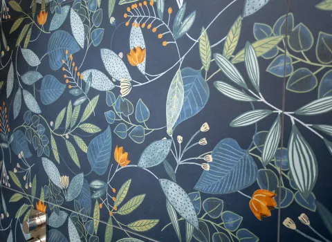 Blumendekor von einer Fliese mit orang-farbenden Blüten und grün/blauen Blättern, der Hintergrund ist blau.