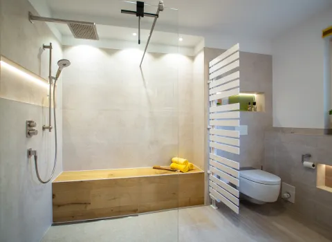 Walk IN Dusche mit langer Sitzbank in Holzoptik und Heizkörper als Raumteiler.