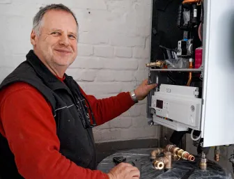 Ein Heizungsmonteur der Firma Laabs wartet eine Gastherme, umgeben von Kupferrohren und Werkzeugen. 