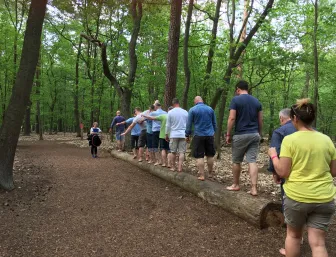 Verschiedene Menschen laufen barfuß über einen Baumstamm.