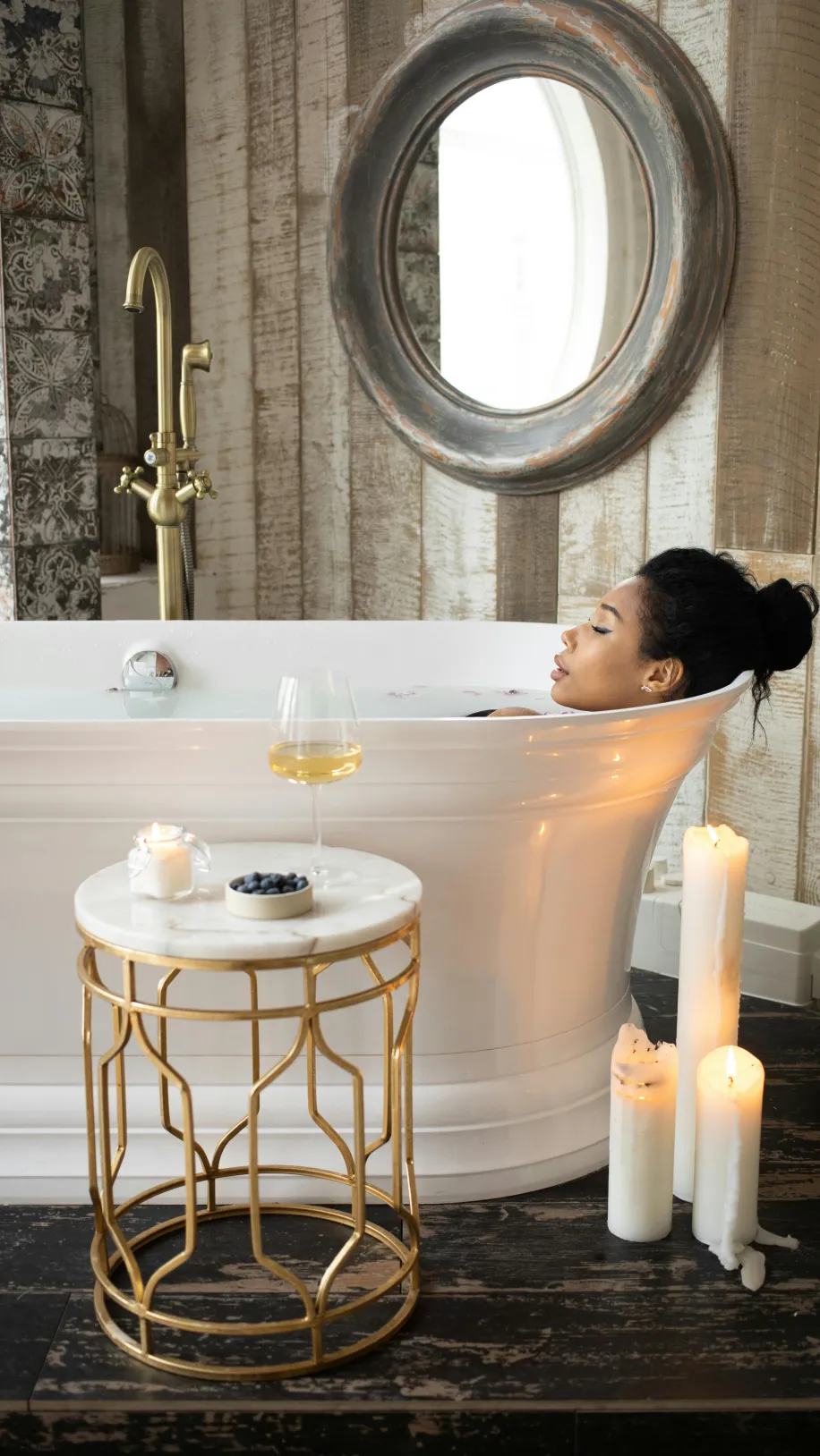 Eine Frau liegt in der Wanne und genießt die Auszeit mit einem Glas Wein und Kerzenschein.