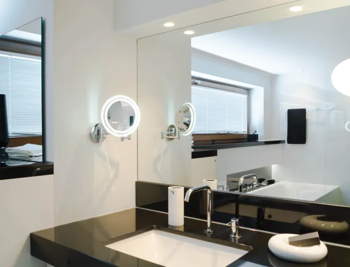 Badreferenz Klassikbad von Laabs mit großer Spiegelwand über schwarzem Waschtisch und rundem Kosmetikspiegel.