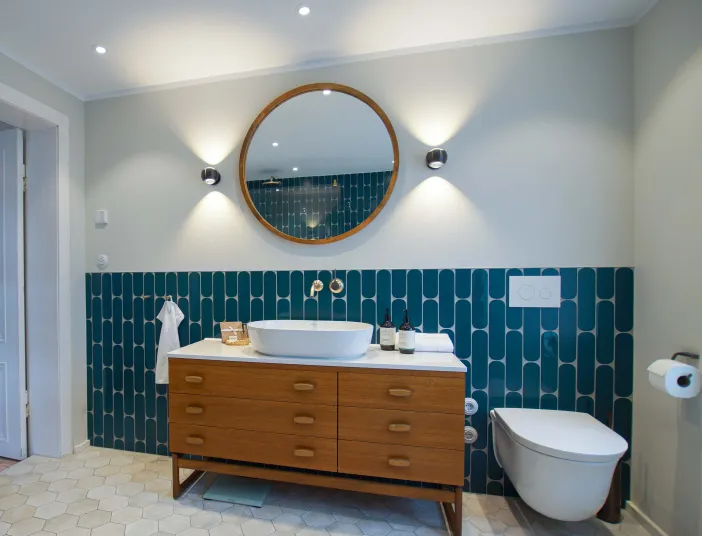 Waschtisch mit rundem Spiegel und WC vor türkisen Fliesen im farbigen Bad vom Handwerksunternehmen bad & heizung Laabs in Potsdam.