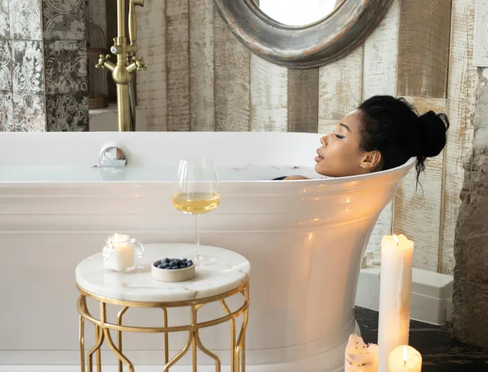 Eine Frau liegt in der Wanne und genießt die Auszeit mit einem Glas Wein und Kerzenschein.