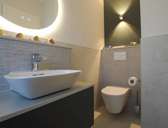 Gästebad mit Aufsatz-Waschtisch und WC mit rundem Lichtspiegel.