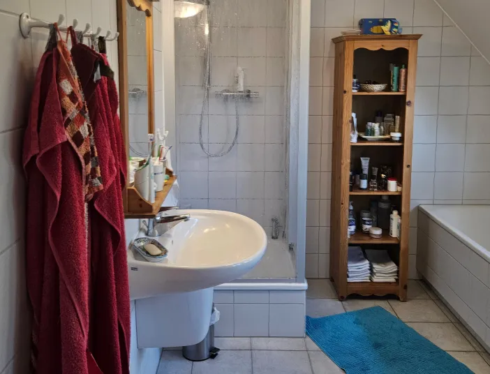 Gewöhnliches Badezimmer mit weißen Standartfliesen im Vordergrund rote Handtücher.